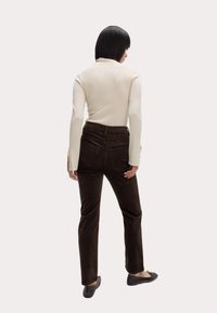 Braune Cordhosen mit Gesäßtaschen, kombiniert mit einem cremefarbenen Langarmoberteil mit Knopfdetails an den Ärmeln.