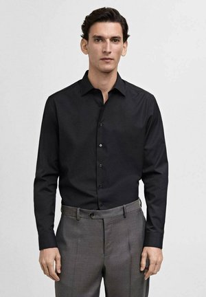 Black, long-sleeve button-up shirt with a classic collar, made of smooth fabric, paired with gray, tailored trousers.