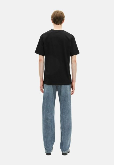 Camiseta de algodón negra con un corte relajado, manga corta y cuello redondo, combinada con unos vaqueros sueltos de color azul claro. Vista trasera simple.