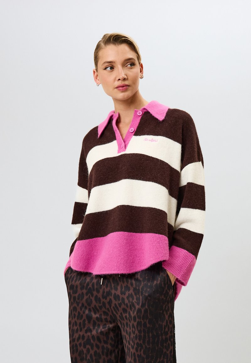 Raidallinen neulepaita ruskean, kermanvärisen ja vaaleanpunaisen sävyissä; siinä on kaulus ja napit, ja se on valmistettu pehmeästä materiaalista rentoa istuvuutta varten.