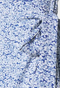 Blumenkleid aus hell- und dunkelblauem Stoff mit kleinem Blumenmuster, weicher Textur und einem gebundenen Taillendetail.