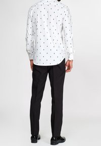 Camicia bianca con bottoni e piccoli motivi di alberi verdi, maniche lunghe e orlo curvo. Abbinata a pantaloni neri e scarpe nere lucide.