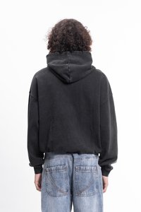 Črna kapuca s širokim krojem in širokimi rokavi, v kombinaciji z svetlo modrimi jeans hlačami, ki imajo opazne zadnje žepe in šiv.
