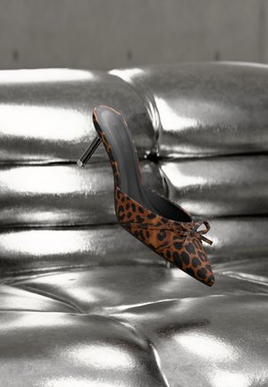 Leopard print high-heeled mule with pointed toe and a small bow, resting on a shiny silver tufted surface.