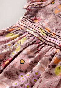 Vestido con estampado floral en tejido rosa suave, con pliegues, mangas cortas y diversas flores en tonos naranja, amarillo y púrpura.