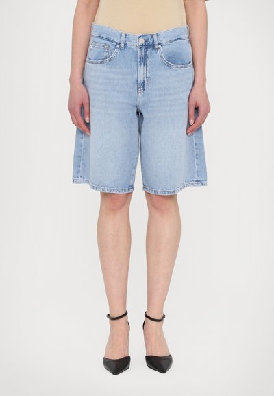 Shorts de mezclilla azul claro con un ajuste relajado, cintura de altura media, bolsillos frontales y dobladillo deshilachado. Combinados con tacones negros de punta afilada.