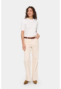 Top bianco a costine con maniche corte abbinato a pantaloni larghi color crema e una cintura in pelle marrone. Stivali alla caviglia marroni completano l'outfit.