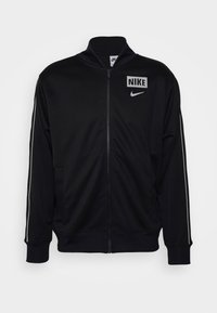 Giacca nera con zip e colletto alto, realizzata in tessuto liscio, con strisce bianche sui lati e un logo Nike quadrato sul petto.