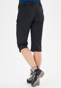 Sorte, knælange udendørs shorts med en tætsiddende pasform og elastisk talje. Båret med grå vandresko med skridsikre såler.