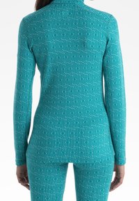 Türkisfarbener Langarm-Top mit tailliertem Design, das ein sich wiederholendes geometrisches Muster in Weiß aufweist. Weicher, elastischer Stoff, der für Komfort sorgt.