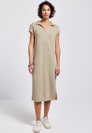 Beiges, geripptes Kleid mit kurzen Ärmeln, Kragen, seitlichen Schlitzen und einem lockeren Schnitt. Kombiniert mit weißen Sneakers für einen lässigen Look.