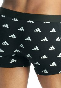 Boxer neri con un motivo a triangoli bianchi ripetuti. Il tessuto è liscio, con una vita elastica nera.