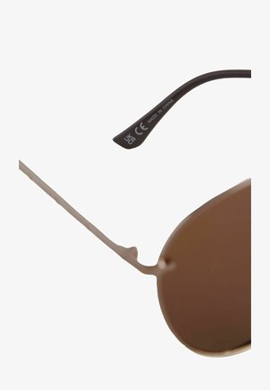 Aviator aurinkolasit ohuella metallikehyksellä, ruskeasti sävytetyillä linsseillä ja mustalla varrella, johon on merkitty "MADE IN CHINA" ja CE-merkki.