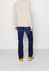 Pull en tricot beige, jean en denim bleu et baskets en toile jaunes. Le pull a un col rond et un ourlet côtelé ; les jeans sont ajustés.