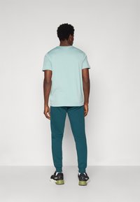 Camisa de manga corta azul claro combinada con pantalones verde azulado oscuro, con un diseño ajustado y puños acanalados, llevada con zapatillas negras y verdes.