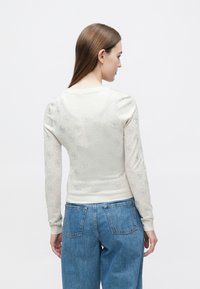 Maglione grigio chiaro con motivo strutturato, maniche lunghe e polsini a coste, abbinato a jeans blu slavati. Design semplice e aderente.