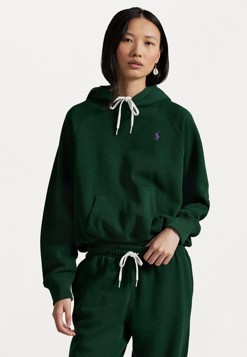 Groene hoodie met witte trekkoorden, voorzak en paarse geborduurde logo. Gekoeld met groene joggers met elastische tailleband.