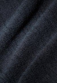 Tessuto nero texturizzato con una superficie morbida e pelosa, che mostra sottili variazioni nella profondità e nella lucentezza del materiale.