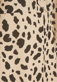 Beige stof met onregelmatige zwarte vlekken die een luipaardprintpatroon vormen.