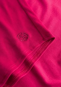 Fuchsia Baumwoll-T-Shirt mit rundem Ausschnitt, Flatlock-Nähten und einem kreisförmigen, tonalen Bestickten Logo in der Nähe des Saums.
