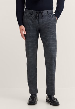 Graue Karohosen mit einem Kordelzugbund, im Slim-Fit-Schnitt und seitlichen Taschen, kombiniert mit schwarzen Loafers. Flacher Frontschnitt.