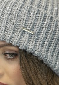 Szary dzianinowy beanie o prążkowanej teksturze z cekinowymi akcentami, z małą srebrną metką logo wszytą z boku.