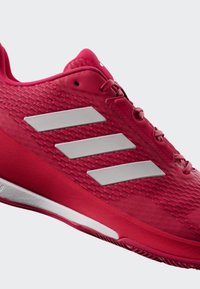 Chaussures de sport rouges avec un dessus texturé, trois rayures argentées métalliques et une semelle en caoutchouc avec un accent blanc.