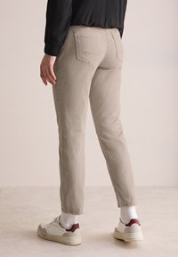 Beige slim-fit byxor i bomullsblandning, med bakfickor, uppvikta nederkanter, och stylade med vita skor och grå strumpor.