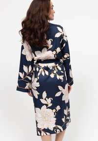 Marineblauwe bloemenkimono met een satijnen afwerking, lange mouwen en een strik taille. Het ontwerp bevat witte bloemen met gouden accenten en heeft een ontspannen pasvorm.