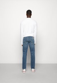 Vit långärmad topp, ljusblå denimjeans och vita sneakers. Jeanssen har synliga bakfickor och rak benform.