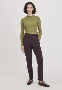 Groen geribbeld truitje en donkerpaarse taps toelopende broek. De outfit heeft een getailleerde silhouette en gladde texturen. Bruine schoenen met een gespdetail.