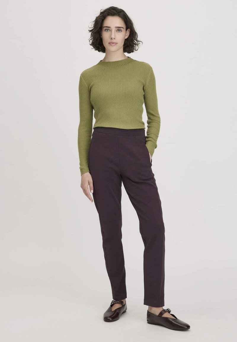 Groen geribbeld truitje en donkerpaarse taps toelopende broek. De outfit heeft een getailleerde silhouette en gladde texturen. Bruine schoenen met een gespdetail.