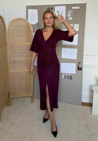 Burgundská, priliehavá midi šaty s výstrihom do V a riasením v oblasti pásu. Sú vybavené širokými rukávmi a bočným rozparkom. V kombinácii s čiernymi ihlovými topánkami.