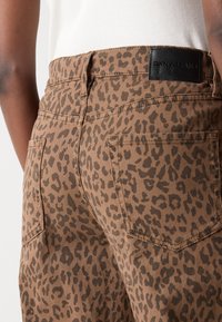 Rudo leopardų rašto džinsai su juodu DKNY Jeans ženklu, užpakaliniais kišenėmis ir tekstūruotu audiniu.