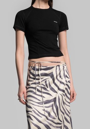 Mujer que lleva una camiseta negra ajustada de manga corta y una falda blanca de cintura alta con rayas negras abstractas de cebra anudada a la cintura.