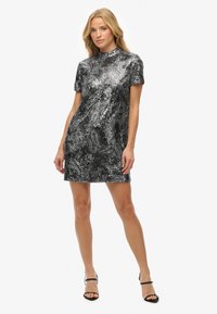 Vestido negro con lentejuelas plateadas de manga corta, con un cuello alto y un patrón texturizado, combinado con sandalias negras de tiras.