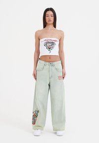 Witte strapless top met tijgerprint; lichtgroene wijde jeans met geborduurde draak en rode tekst aan de voorkant.