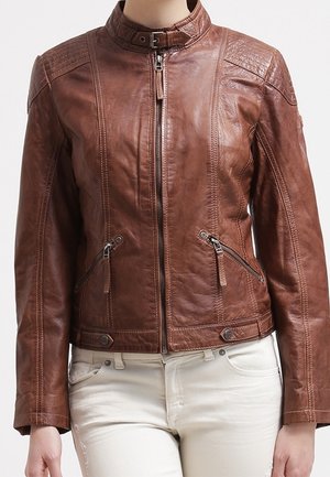 Veste en cuir marron avec fermeture éclair à l'avant, poches latérales zippées et col à bouton-pression, portée avec un pantalon de couleur claire.