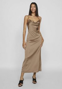 Een bruin satijnen slipdress met spaghettibandjes, voorzien van een halslijn met plooien en een rechte silhouet. Gedragen met zwarte open teen hakken.