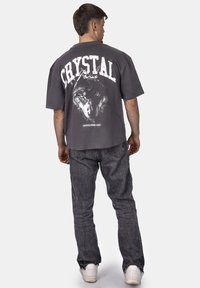 Šedé oversized tričko s grafickým motivem vlka a textem "CRYSTAL" na zádech. Nosené s tmavě šedými džíny a bílými teniskami.