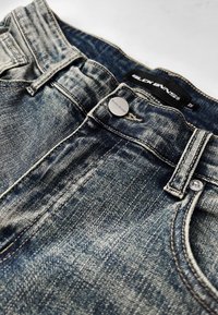 Mörkblå jeans i denim med dragkedja, silverfärgad knappstängning och en svart etikett med "BLCK BNNS" på midjebandet.