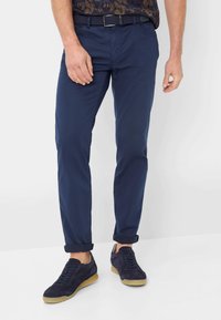 Marinefarbene Chinos aus leichtem Stoff mit geradem Schnitt, ausgestattet mit aufgerollten Säumen und seitlichen Taschen, kombiniert mit dunkelblauen Wildledersneakern.