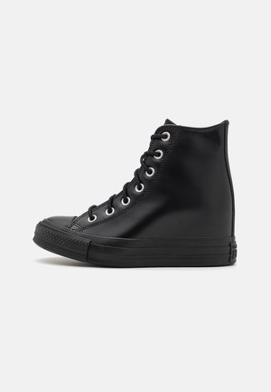 Zapatilla negra de caña alta con cordones en la parte delantera, suela de goma y ojales metálicos, mostrada de perfil sobre un fondo blanco.