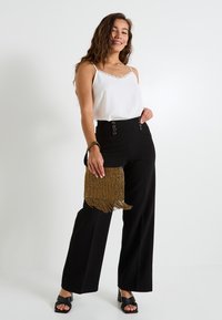 Camiseta blanca con encaje, pantalones negros de cintura alta con accesorios circulares y un bolso dorado con cuentas y flecos. Sandalias negras de tacón.