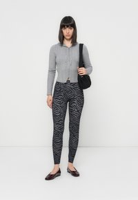 Gray knitted cropped hoodie with a front zipper, paired with black and gray zebra-patterned leggings and glossy burgundy flats.