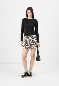 Maglietta nera a maniche lunghe abbinata a una gonna bianca con stampa animale marrone e nera, completata da sneakers nere e una piccola borsa nera.