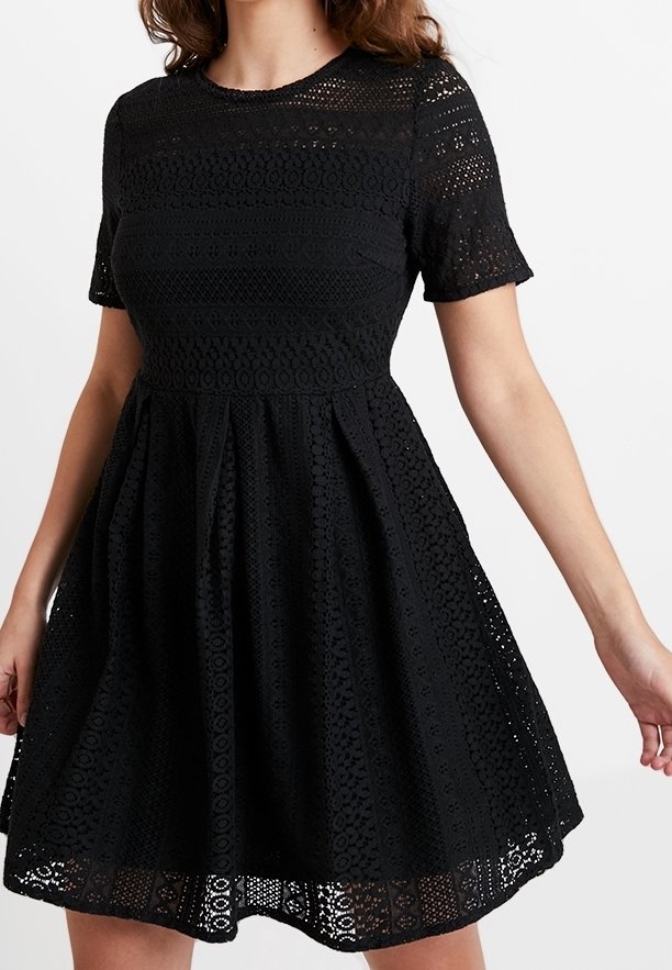 Schwarzes, kurzärmliges Kleid aus strukturiertem Spitze-Material. Es hat ein tailliertes Oberteil und einen ausgestellten Rock, mit einem gemusterte Saumlinie und rundem Ausschnitt.