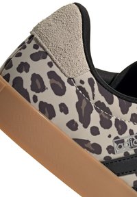 Gros plan d'une basket avec imprimé léopard gris et noir, patch en daim beige au talon, bordure noire et semelle en caoutchouc marron clair.