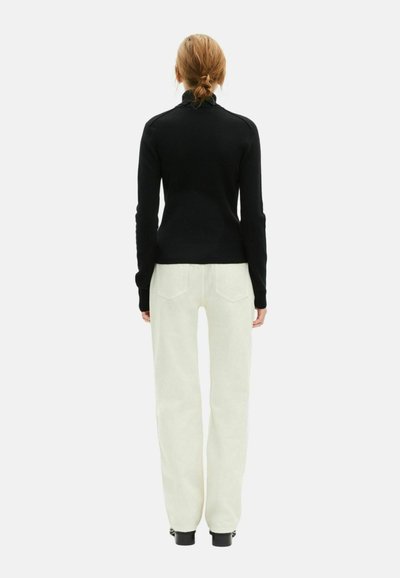 Suéter negro ajustado con cuello alto, combinado con pantalones anchos blancos y botas negras hasta el tobillo; textura suave, diseño simple.