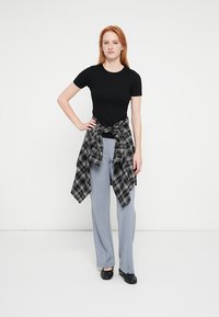 Sort kortærmet T-shirt, grå vidde bukser, sort-hvid ternet skjorte bundet om livet, flade sorte sko.